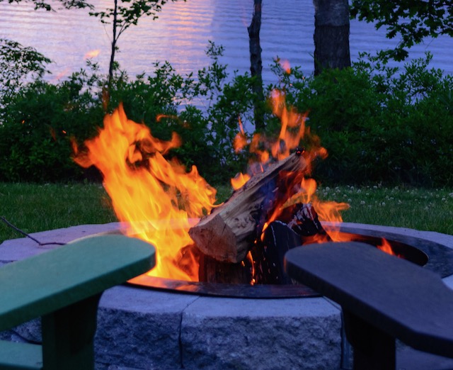 Roaring fire in an outdoor fire pit with a lake in the background